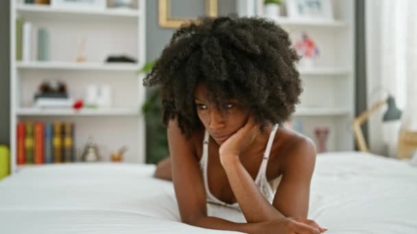 Африканская американка лежит на кровати и выглядит сексуально, думая в спальне. - Кадры, видео