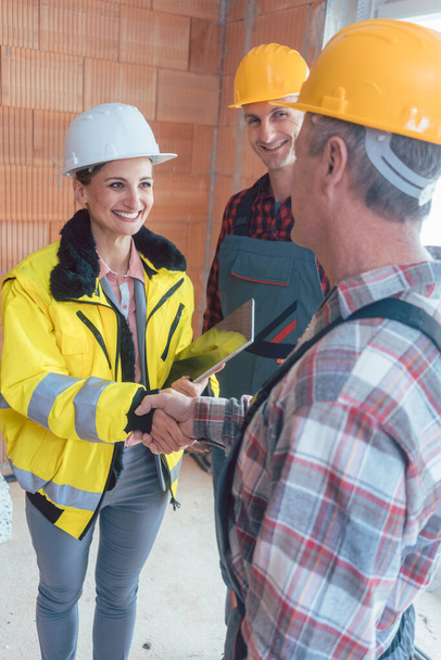 Smiling female contractor with tablet computer shaking hand of senior builder before starting work - Photo, Image