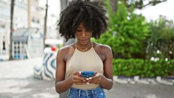 Mujer afroamericana usando smartphone sonriendo en el parque - Metraje, vídeo
