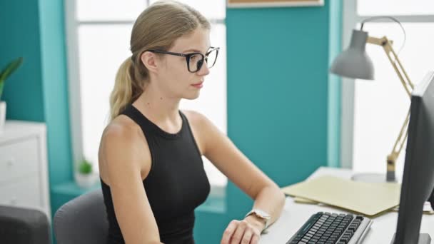 Młoda blondynka biznes pracownik za pomocą komputera uśmiechając się w biurze - Materiał filmowy, wideo