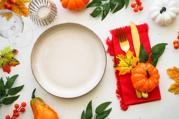 Autumn table setting at white kitchen table. Craft plate, golden cutlery and fall decorations with pumpkins and leaves. Flat lay image with copy space. - Photo, Image