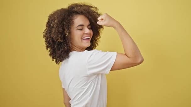 Giovane bella donna ispanica sorridente fiducioso facendo gesto forte con braccio su isolato sfondo giallo - Filmati, video