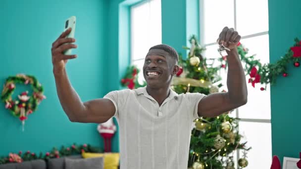 Afrikkalainen amerikkalainen mies juhlii joulua ottaa videopuhelu tilalla avain kotona - Materiaali, video