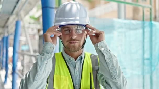Nuori valkoihoinen mies arkkitehti hymyilee luottavainen ottaen lasit rakennuspaikka - Materiaali, video