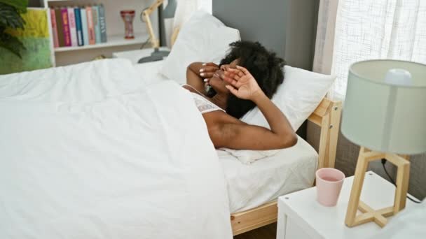Mujer afroamericana despertando usando camisón en el dormitorio - Imágenes, Vídeo