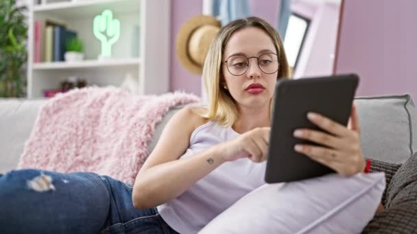 Mujer rubia joven de compras con touchpad y tarjeta de crédito sentado en el sofá en casa - Metraje, vídeo