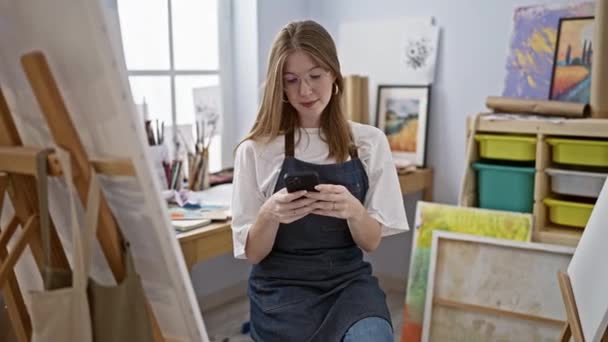 Mladé blondýny žena umělec pomocí smartphone v art studio - Záběry, video