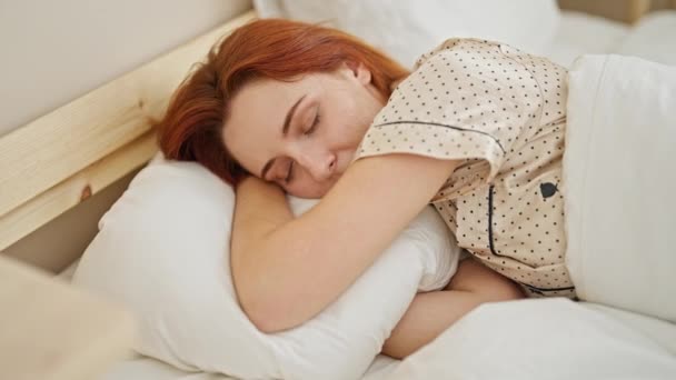 Nuori punapää nainen hymyilee luottavainen makaa sängyssä makuuhuoneessa - Materiaali, video