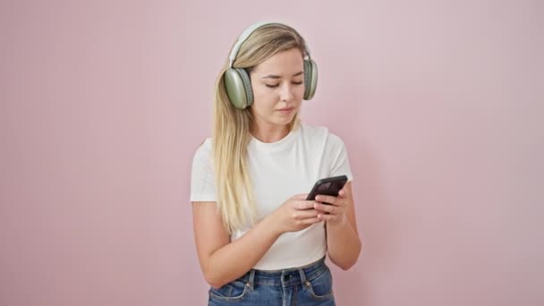 Mladá blondýna žena poslouchá hudbu a tanec přes izolované růžové pozadí - Záběry, video