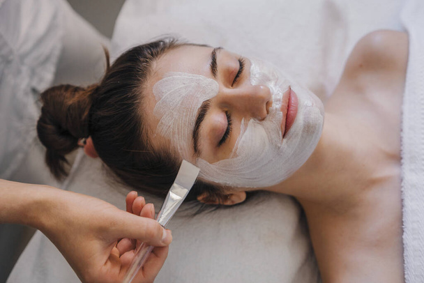 Young woman receiving nourishing face mask with particles atr spa salon. Beautiful woman face skin care. Facial treatment. Cosmetic procedure. Healthy lifestyle - Photo, Image