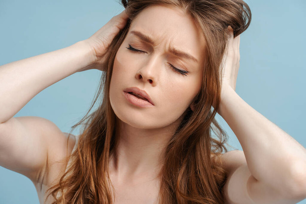 Closeup portrait of sad woman holding head, having headache, stress isolated on blue background. Unhappy girl with closed eyes painful. Concept of migraine, treatment - Foto, afbeelding