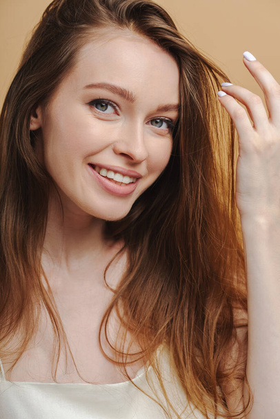 Ritratto di bella donna dai capelli lunghi che sorride guardando la macchina fotografica isolata su sfondo beige. Attraente ragazza positiva in posa in studio. Concetto di assistenza sanitaria, cure dentistiche - Foto, immagini