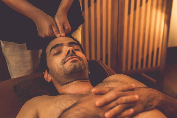 Uomo caucasico godendo rilassante anti-stress massaggio alla testa e coccole bellezza del viso svago della pelle in calda candela illuminazione ambiente salone spa in resort di lusso o hotel. Silenzioso - Foto, immagini
