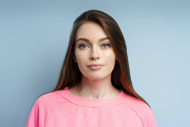 Portrait de belle femme intelligente portant un sweat-shirt rose regardant la caméra. Jeune femelle posant en studio isolé sur fond bleu. Concept d'éducation - Photo, image