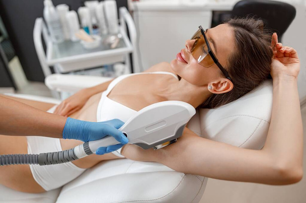 Žena klient v brýlích během podpažní fotografie epilace postup s ipl stroj v salonu krásy. - Fotografie, Obrázek
