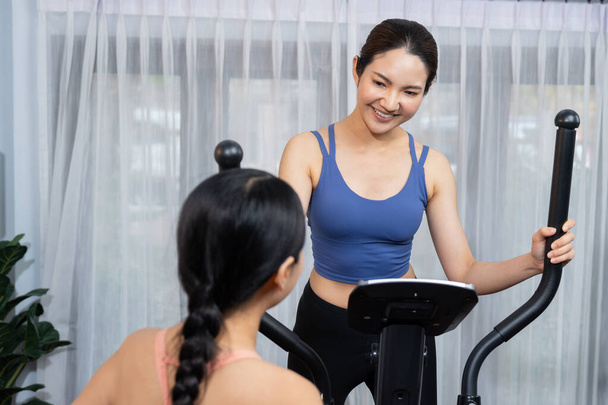 Energinen ja vahva urheilullinen aasialainen nainen käynnissä elliptinen käynnissä kone kotona harjoitus kaveri tai kouluttaja. Sopivan ruumiinrakenteen tavoittelu ja sitoutuminen terveelliseen elämäntapaan. Voimakas - Valokuva, kuva