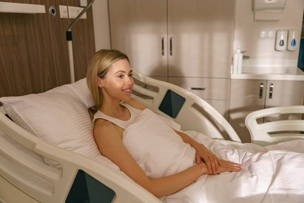 Junge Frau liegt nach Operation auf moderner Krankenstation im Bett Hochwertiges Foto - Foto, Bild