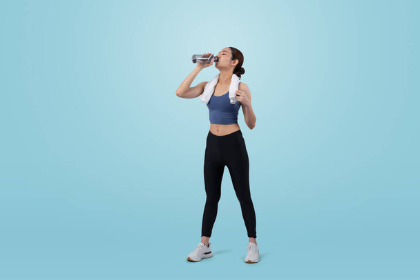 Athletic and sporty asian woman resting and drink water after intensive cardio workout training. Healthy exercising and fit body care lifestyle pursuit in studio shot isolated background. Vigorous - Photo, Image