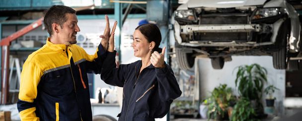Two happy vehicle mechanic celebrate and high five after made successful car inspection or repair in automotive service car workshop. Technician team enjoy accomplishment together. Panorama Oxus - Photo, Image