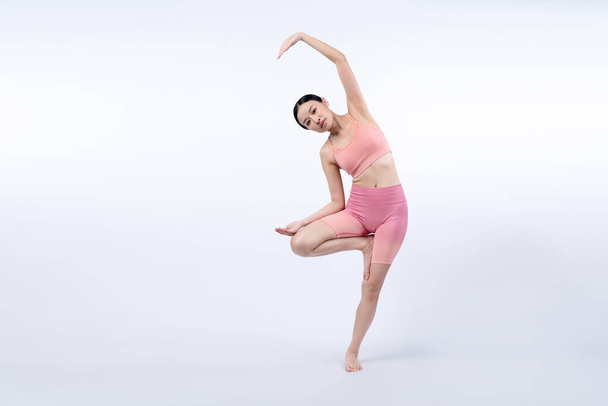 Mujer asiática en ropa deportiva haciendo ejercicio de yoga en pose de pie en la aptitud como su rutina de entrenamiento. Cuidado corporal saludable y meditación yoga estilo de vida en plena toma sobre fondo aislado. Vigoroso - Foto, Imagen