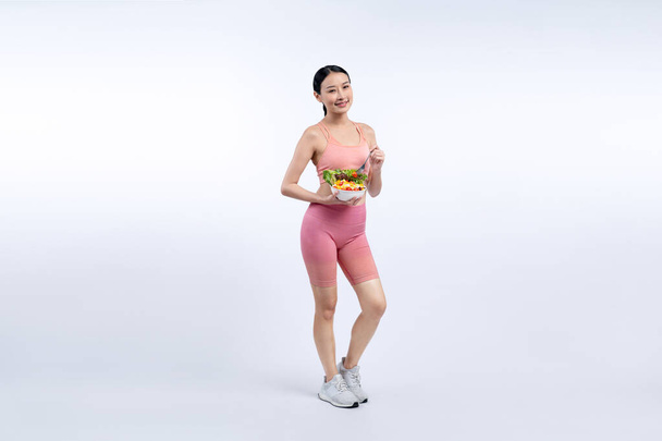 Молода спортивна азіатка в спортивному одязі, що тримає салатну чашу, наповнена яскравими фруктами та овочами. Природний молодіжний спосіб життя тіла з балансовим харчуванням на ізольованому фоні. Яскравий - Фото, зображення
