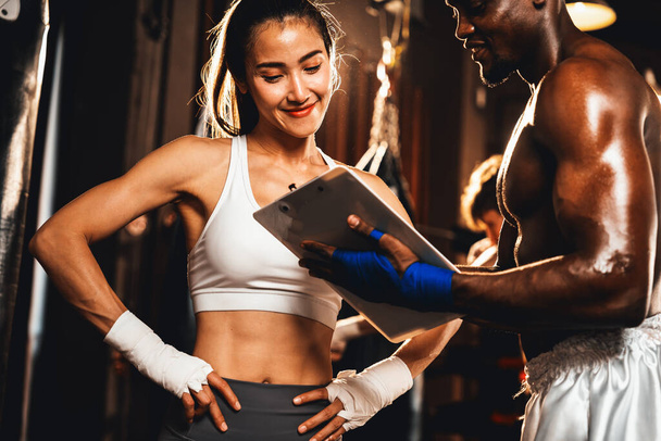 Азійка муай тай-боксер і її особистий тренер з боксу обговорюють її фізичний прогрес у спортзалі, що відображає прихильність росту її м'язів і боксу. Імпест - Фото, зображення