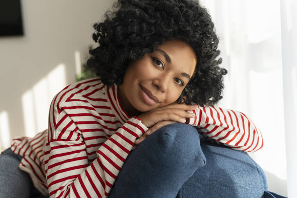 Porträt der schönen lächelnden Afroamerikanerin mit lockigem Haar, die zu Hause in die Kamera schaut - Foto, Bild