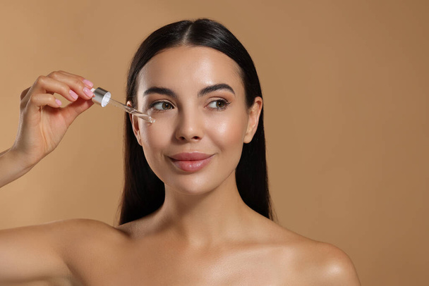 Beautiful young woman applying serum onto her face on beige background. Space for text - Foto, afbeelding