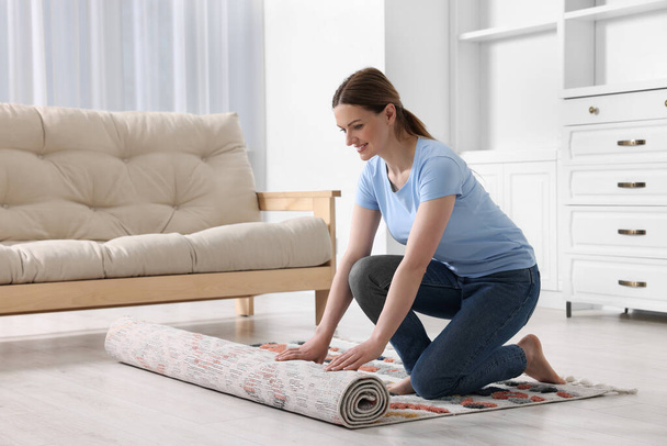 Smiling woman unrolling carpet with beautiful pattern on floor in room - Φωτογραφία, εικόνα