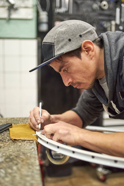 Jovem hispânico preparando uma roda de bicicleta com fita adesiva para pintar em sua oficina. - Foto, Imagem