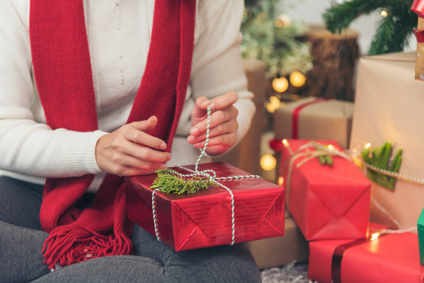Közelkép női kéz csomagolja ajándék kényelmes nappaliban. A nő karácsonyi ajándékdobozt csomagol a karácsonyfa alá. Ázsiai nő dekoráció csecsebecse labda karácsonyfa a karácsonyi ünnep tél szezonális ünnep - Fotó, kép