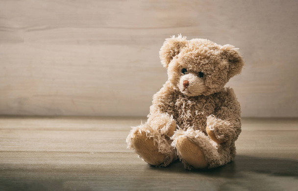 Teddybär sitzt auf einem leeren Holzboden. Braunes einsames, trauriges Plüschtier auf Holztisch. Geburtstag, Valentinstag, Weihnachtsgeschenk. Kopierraum - Foto, Bild