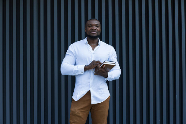 Nuori, menestynyt afroamerikkalainen mies, jolla on muistikirja ja älypuhelin käsissään. - Valokuva, kuva