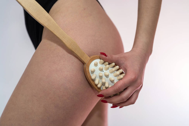 Молодая женщина держит антицеллюлитный массаж сухой щеткой возле ног. Лечение  - Фото, изображение
