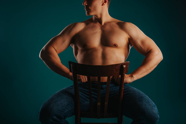 Δυνατός, γυμνασμένος, αρρενωπός εραστής που δείχνει τον όμορφο κορμό του ενώ κάθεται σε μια καρέκλα - Φωτογραφία, εικόνα