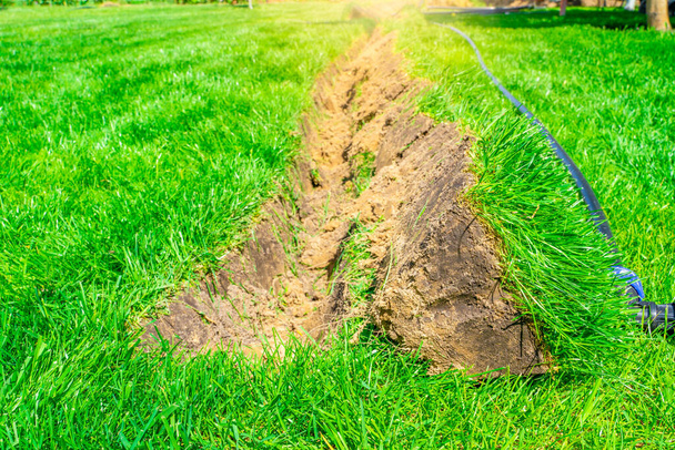 A ditch dug in the lawn for laying pipes and installing irrigation. Soil under green lawn and grass root system - Photo, Image