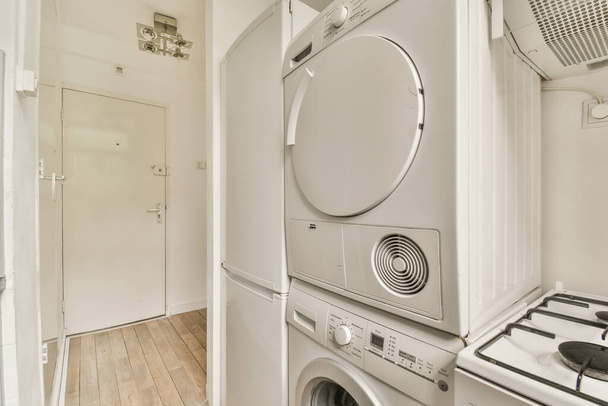 pesukone ja kuivausrumpu pesuhuoneessa, jossa on puulattia, valkoiset seinät ja kaapit molemmin puolin - Valokuva, kuva