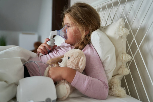 Ragazza in età elementare utilizzando nebulizzatore a letto a casa - Foto, immagini