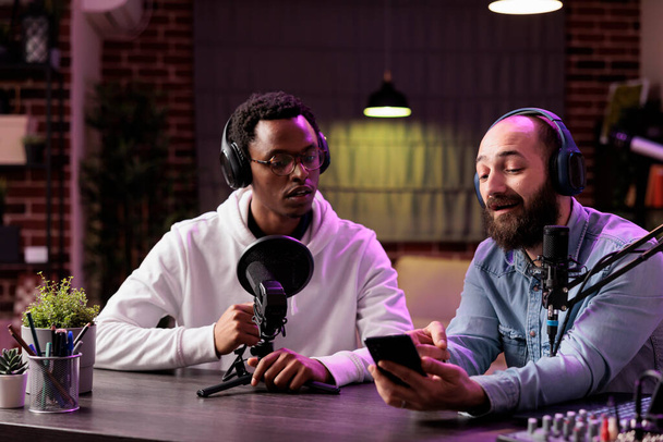 Content maker filmen podcast aflevering tonen Afrikaanse Amerikaanse beroemdheid gast op smartphone vragen ontvangen van het publiek. Vlogger verbindende man met zijn fans van home studio - Foto, afbeelding