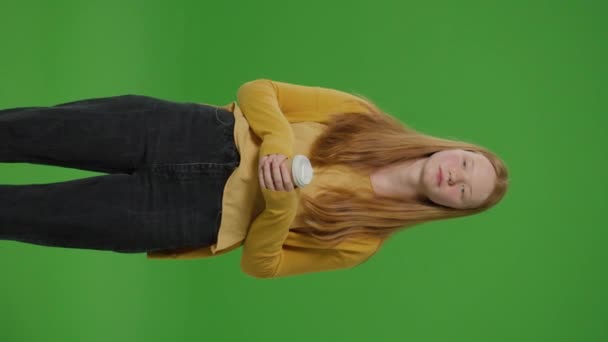 Green Screen. Vertical Video Серйозна дівчина-підліток стоїть тримаючи чашку кави відображаючи глибокі думки. Її голодна позиція і орієнтований вираз запропонувати момент споглядання серед робочого дня - Кадри, відео