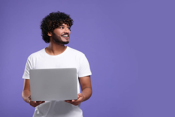 Smiling man with laptop on purple background, space for text - Fotó, kép