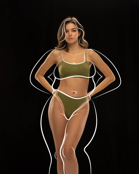 Pretty woman in khaki lingerie with drawn white silhouette around body posing against black background. body positivity. Concept of healthy eating, sport, diet, body care. Black mode. copy space. - Photo, Image