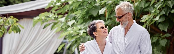 allegro uomo maturo con tatuaggio che abbraccia moglie in occhiali da sole e accappatoio, giardino estivo, banner - Foto, immagini