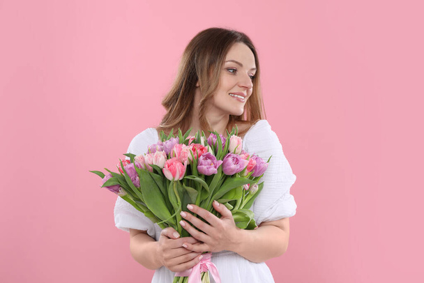 Happy young woman with bouquet of beautiful tulips on pink background - Fotó, kép