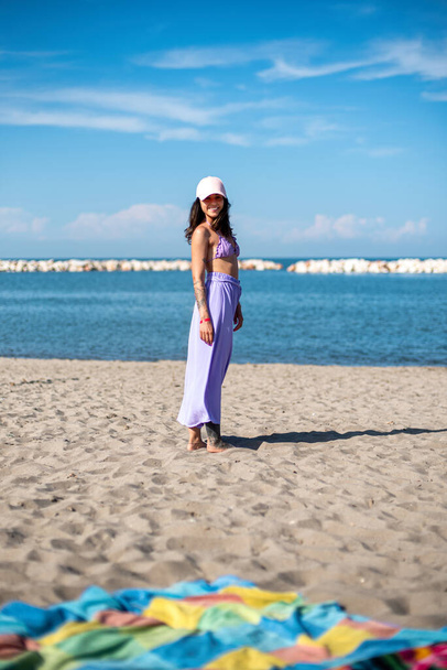 Glimlachend getatoeëerd meisje, poserend op het strand voor de blauwe zee - Foto, afbeelding