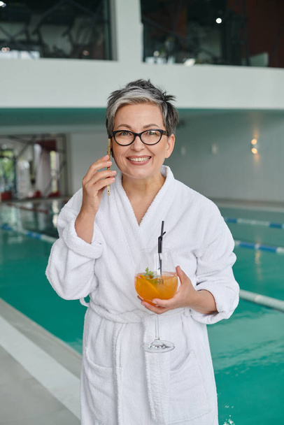 wellness spa concept, happy mature woman in glasses holding cocktail and talking on smartphone - Photo, Image