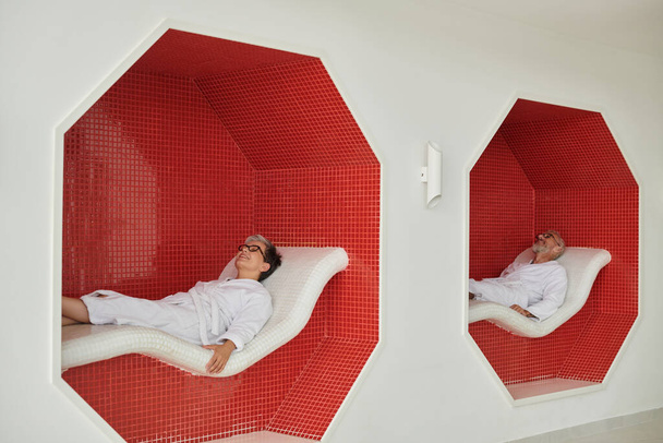 Spa inziva konsepti, beyaz cüppeli ve gözlüklü, dinlenme odasında dinlenen olgun bir çift. - Fotoğraf, Görsel