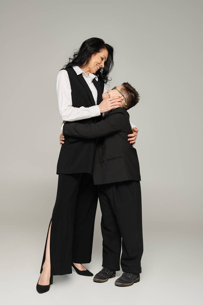 Junge mit Down-Syndrom, in Schuluniform und Frau in offizieller Kleidung umarmen graue, einzigartige Familie - Foto, Bild