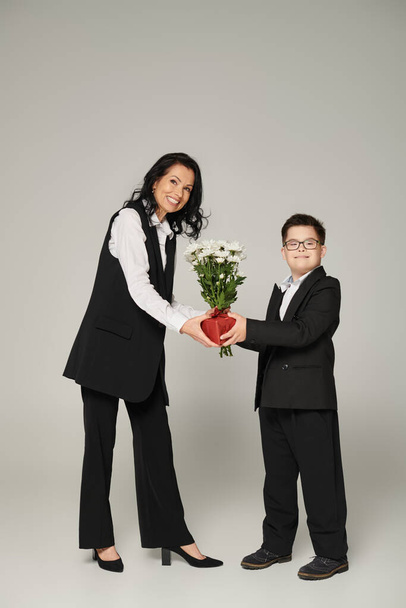 szczęśliwy businesswoman i syn z zespołem Downa trzymając pudełko i kwiaty na szarości - Zdjęcie, obraz