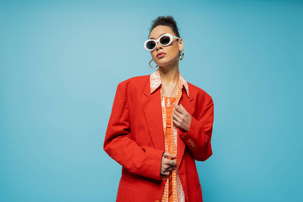 portrait of stylish african american woman in trendy accessories and vibrant outfit posing on blue - Photo, Image